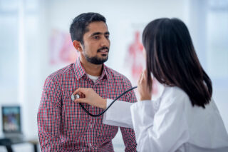 photo - Doctor Sits across from Patient and Using a Stethoscope Listens to His Heart