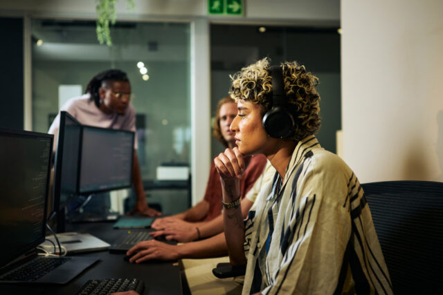 photo - Female Programmer Working on Code in Busy Office with Headphones